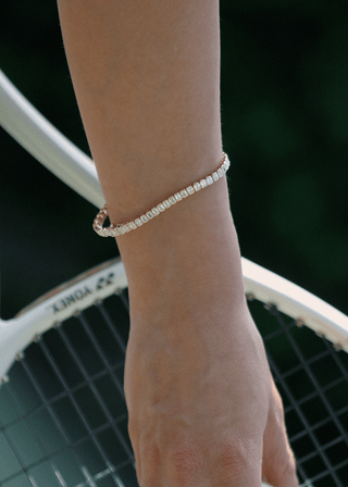 Emerald cut bezel lab grown diamond tennis bracelet worn on wrist beside a tennis racket.