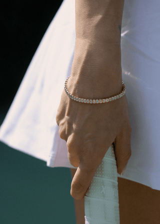 Emerald cut bezel lab grown diamond bracelet worn on wrist holding a tennis racket.