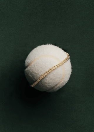 Emerald cut bezel lab grown diamond bracelet on a tennis ball against a green background.